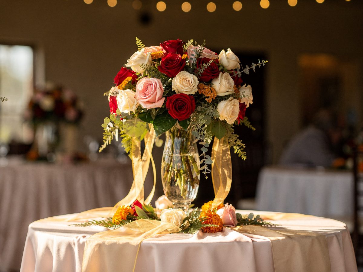 Tall quinceanera centerpiece with red and blush roses and marigold accents
